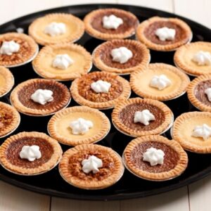 A tray full of assorted tarts topped with whipped cream.