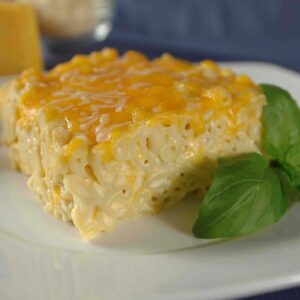 A large square of macaroni and cheese on a plate with a garnish of basil.